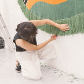 Person hanging a large decorative tapestry with green, orange, and black colors.